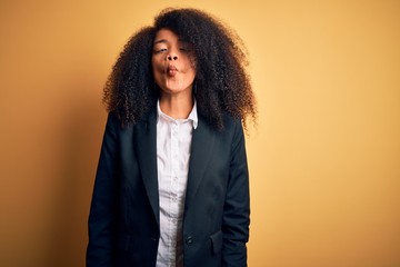 Young beautiful african american business woman with afro hair wearing elegant jacket making fish face with lips, crazy and comical gesture. Funny expression.