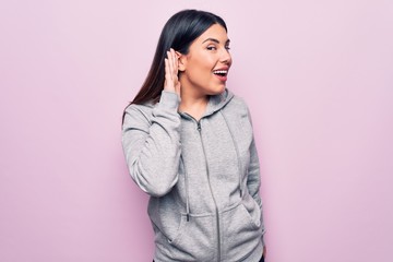 Sticker - Young beautiful sporty woman wearing sportswear standing over isolated pink background smiling with hand over ear listening and hearing to rumor or gossip. Deafness concept.