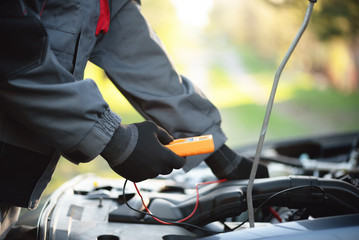 Canvas Print - Worker with multimeter near open car hood. Auto electrician.