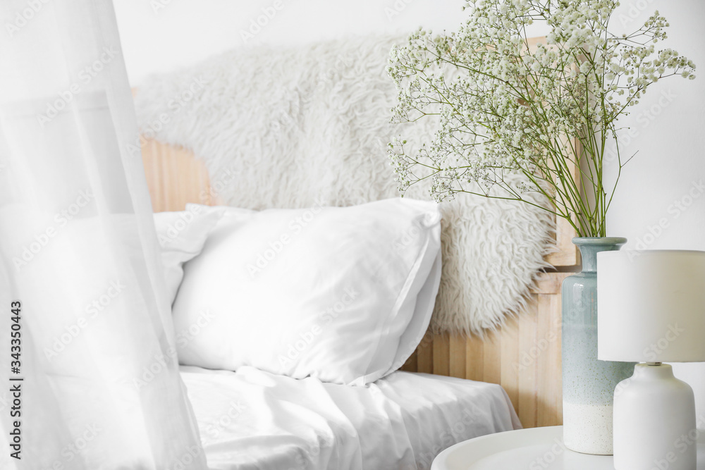 Vase with flowers on table in bedroom