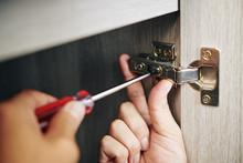 Close-up Image Of Handyman Assembling Kitchen Cabinet And Screwing Door Hinge
