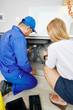 © DragonImages - Young woman showing repairman leaky drain under kitchen sink