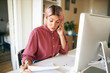 © shurkin_son - Confident young businesswoman working from home because of social distancing, sitting in front of computer, holding sheet of paper, discussing financial report with manager, having phone call