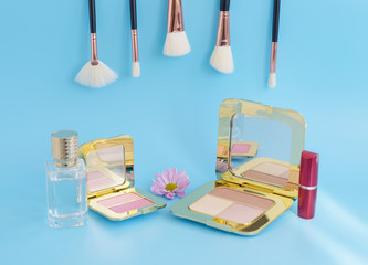 premium makeup brushes, red lipstick, bottle of perfume and blush pads on a bright blue background, creative cosmetics flat lay