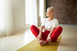 © shurkin_son - Attractive cheerful retired woman in sportswear sitting on yoga mat with knees bent, pressing soles of feet together doing baddha konasana. People, healthy lifestyle, activity and wellness concept