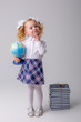 © Olesya Pogosskaya - a small curly haired blonde girl in a school uniform holds a globe in her hands thinking on a white background