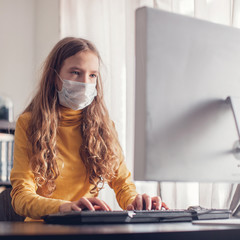 Teen gaming at home with computer, wearing protective mask