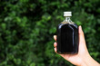 women hand holding cold brew coffee bottle on green nature blurred background
