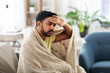 health, cold and people concept - sick young indian man in blanket having headache or fever at home