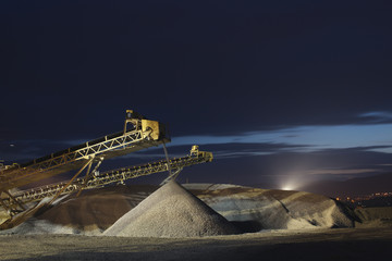 Wall Mural - Rock stone crushing machine conveying crushed rocks at the mining enterprise illuminated by spotlights at night. Heavy mining equipment.