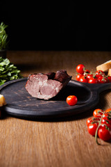 Wall Mural - selective focus of tasty ham on board near parsley, cherry tomatoes and baguette on wooden table isolated on black