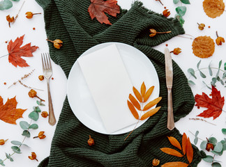 Wall Mural - Table setting with autumn leaves, floral decor and green napkin on white background . Top view, flat lay