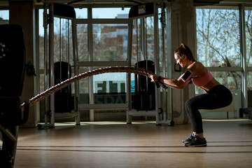 Wall Mural - Young woman with battle ropes exercise in the fitness gym