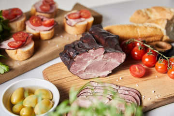 Wall Mural - selective focus of tasty ham on cutting board with cherry tomatoes, olives and baguette near canape