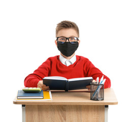 Sticker - Little schoolboy in protective mask sitting at desk on white background. Concept of epidemic