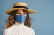 Woman wearing trendy spring, summer fashion outfit during quarantine of coronavirus outbreak. Model dressed protective stylish handmade face mask, straw hat, white blouse, earrings. Copy, empty space