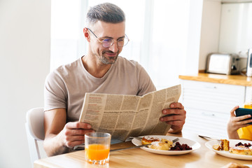 Wall Mural - Photo of man reading newspaper while having breakfast with his daughter