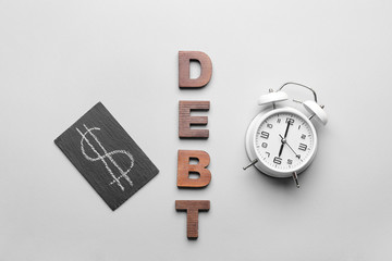 Word DEBT with alarm clock and dollar symbol on grey background