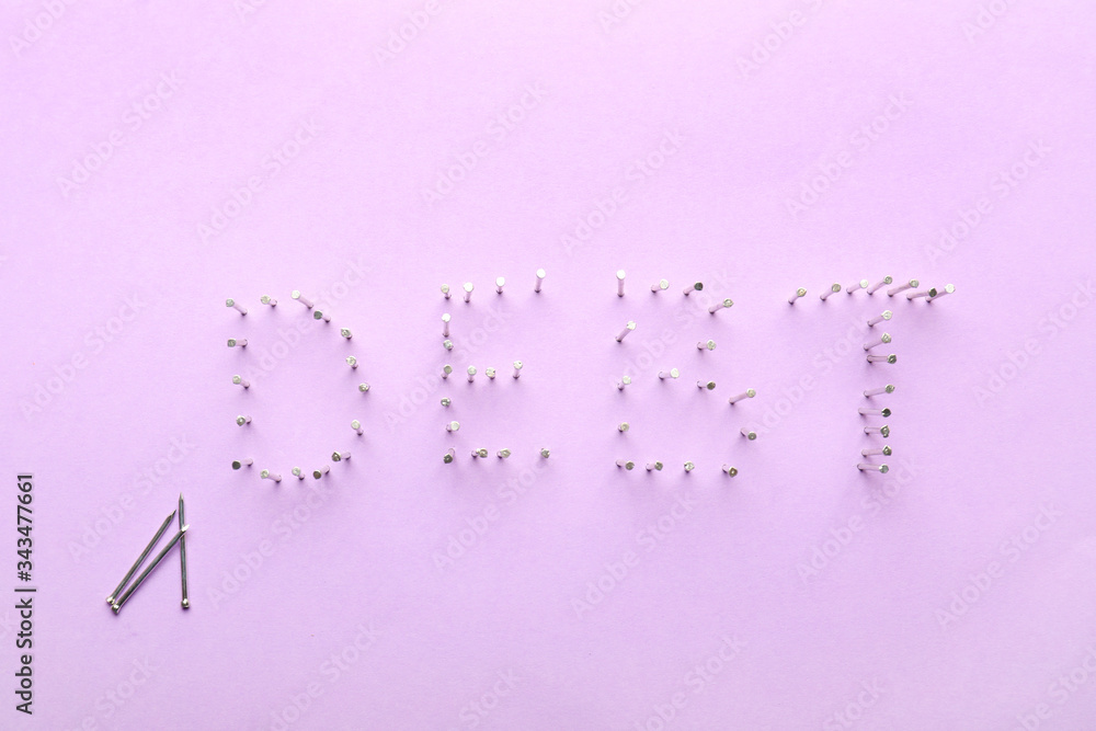 Word DEBT made of nails on color background