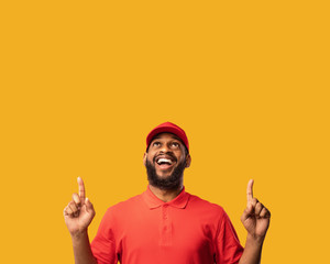 Wall Mural - Delivery Man Pointing Fingers At Copy Space Over Yellow Background