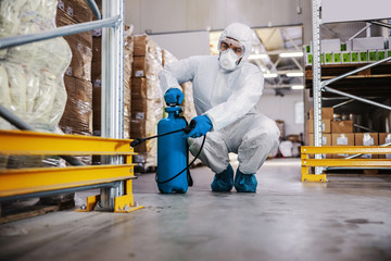 Wall Mural - Man in protective suit and mask disinfecting warehouse full of food products from corona virus / covid-19.