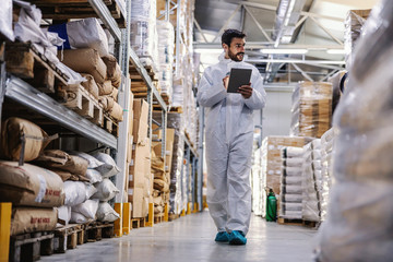 Wall Mural - Full length of worker in protective sterile uniform walking trough warehouse and checking sterilization from corona virus.