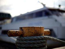 Close-up Of Mooring Bollard With Boat In Background At Harbor