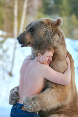 half-naked caucasian man hugs a brown bear in a winter forest. bear hugs man in response. vertical p