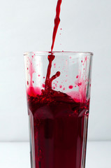 Splashing liquid red pomegranate and grape juice pouring into a glass