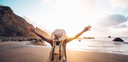 Happy woman with arms up enjoy freedom at the beach at sunset. Wellness, success, freedom and travel concept