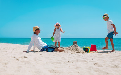 father with laptop trying to work and kids play with sand on beach