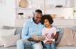 © Prostock-studio - Lockdown hobbies. Mature African American man reading fairy tale to his granddaughter at home