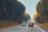 Fototapeta Sawanna - Traffic in high speed on a highway through rural landscape on sunset.
