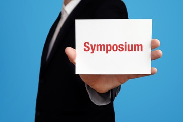 Symposium. Business man in a suit holds card at camera. The term Symposium is in the sign. Symbol for business, finance, statistics, analysis, economy