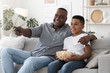 © Prostock-studio - Happy African American Grandfather Watching TV With Grandson At Home Together