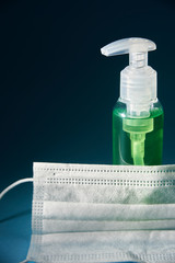 green hand sanitizer bottle and medical face mask. dark background