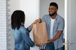 © Prostock-studio - Grocery Delivery. Smiling Black Courier Delivering Order To Young Woman's Home