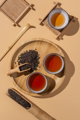 Wall Mural - Tea ceremony in minimalism style, black puer tea in ceramics bowls,dry pu-erh tea leaves in a wooden bamboo spoons and plate on a beige background.