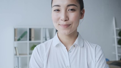 Wall Mural - A charming happy calm young asian businesswoman is looking and smiling to the camera while sitting in the office