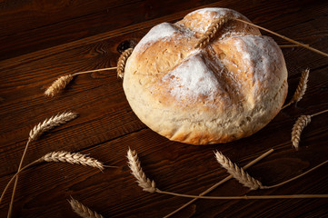 Homebaked bread. Round Loaf Peasant bread and ears of wheat on the wooden background.