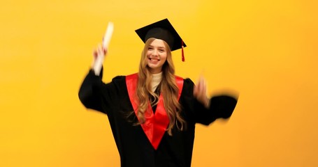 Wall Mural - graduate girl with a diploma, shows a gesture of victory and success, on a yellow background, celebrating graduation from the University, dancing, party
