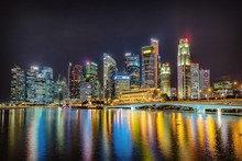 Illuminated Singapore Cityscape Against Calm Sea At Night