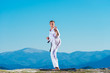 Blond karate athlete does kata on top of a mountain while performing a line up of kicks, punches and blocks on top of a mountain on a sunny day.