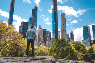 Young man exploring Central Park in New York city on a warm sunny day by the main pond surrounded with skyscrapers