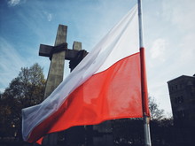 Low Angle View Of Polish Flag By Cross Against Sky In City