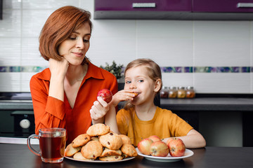 Difficult choice between healthy and unhealthy food during quarantine, isolation at home. Mother and daughter in the kitchen. A little girl eats delicious homemade cookies. 