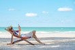 Young smart Asian man tourism in sunglasses relaxing and lying on beach chair on tropical island beach using smartphone with internet for working or online shopping in summer holiday vacation trip.