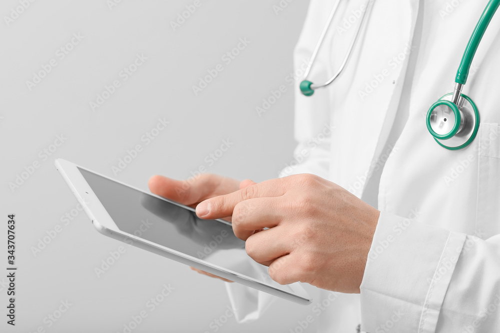 Male doctor with tablet computer on light background, closeup