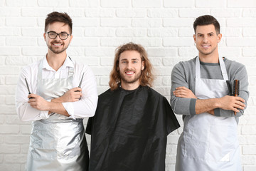 Wall Mural - Young hairdressers with model on white brick background