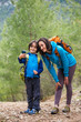 © zhukovvvlad - A child with a backpack takes a selfie on a smartphone with mom on the background of a mountain forest.